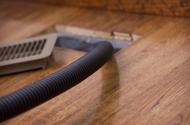 Detail image of a vacuum hose in an air duct for cleaning. Focus is on the hose.